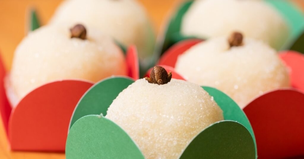 Beijinhos cobertos com coco ralado e cravinho no topo, servidos em forminhas coloridas, comida de festa junina doce.