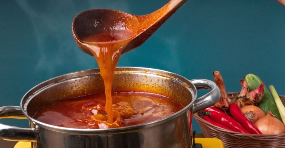 Panela com feijão cozido, mostrando caldo encorpado e grãos visíveis, sendo mexido com colher de pau.