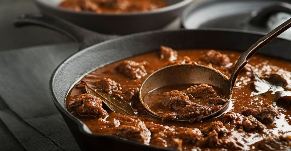 Carne em pedaços sendo estufada com legumes em uma panela funda e tampada.