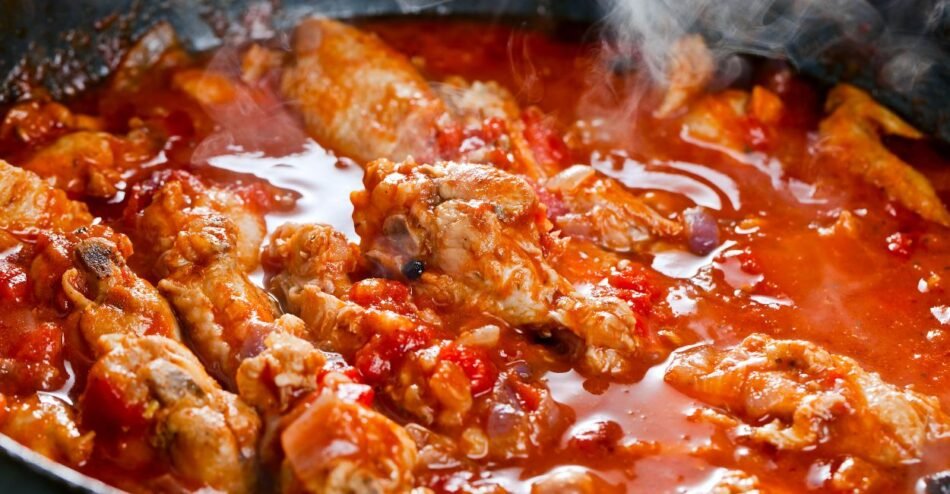 Frango cozinhando lentamente em panela tampada com legumes e molho.
