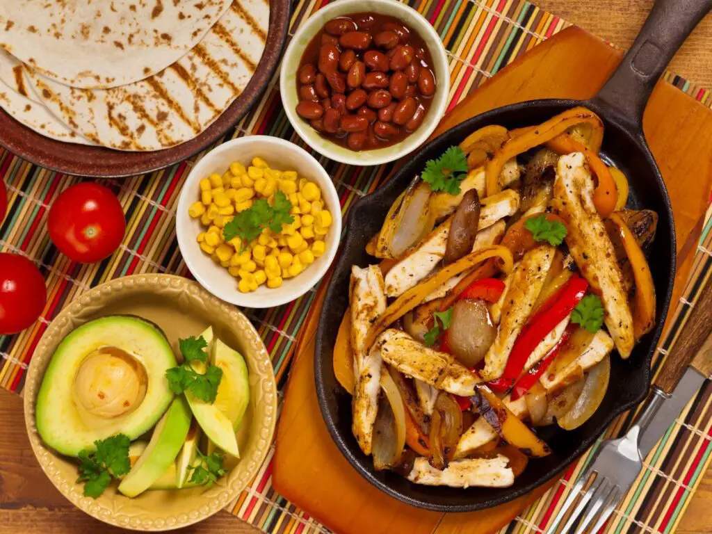 Comidas com F: Fajitas de carne grelhada, pimentões coloridos e cebolas, servidas em uma frigideira de ferro quente.