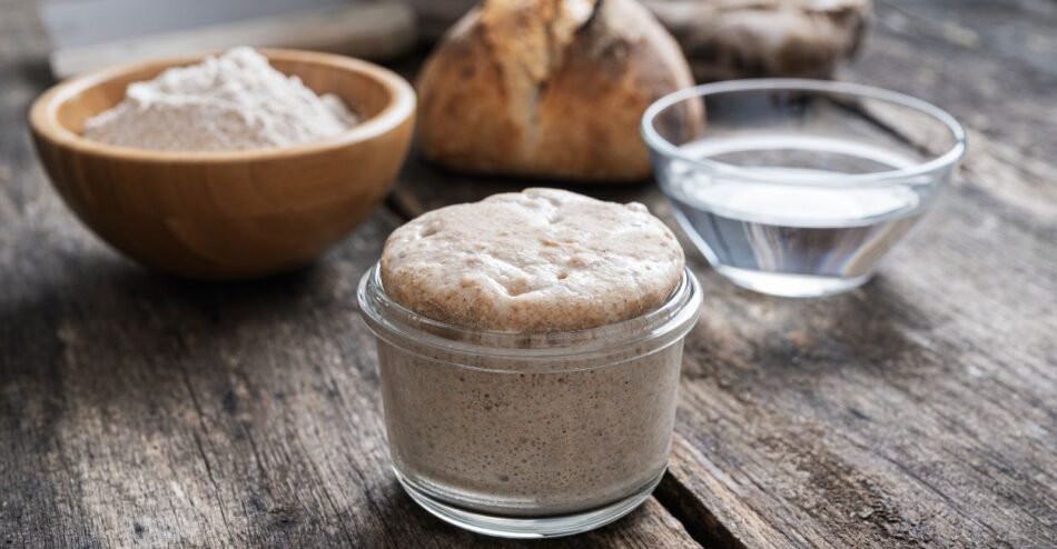 Pão fermentado fresco com textura aerada em fatias sobre uma tábua de madeira.