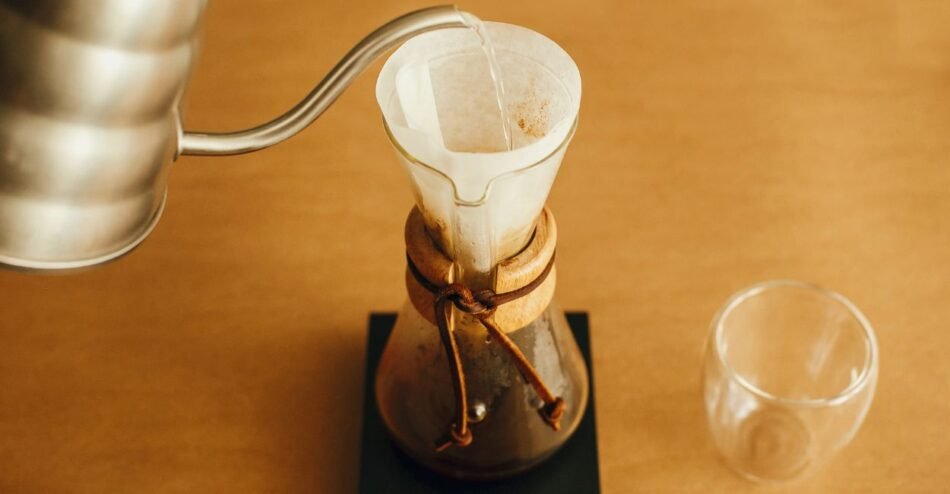 Barista filtrando café manualmente com jarra de vidro sobre balança.