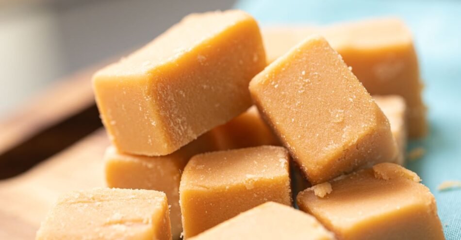 Quadradinhos de fondant de leite dispostos sobre uma tábua de madeira, com leve cristalização visível.