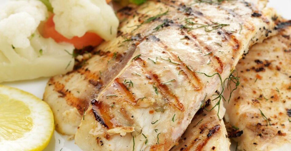 Filé de peixe grelhado servido com legumes salteados e limão fatiado.