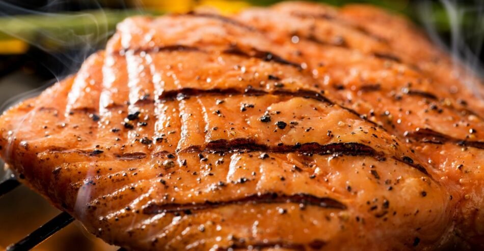 Filé de salmão grelhado com crosta dourada, servido com limão e legumes salteados.