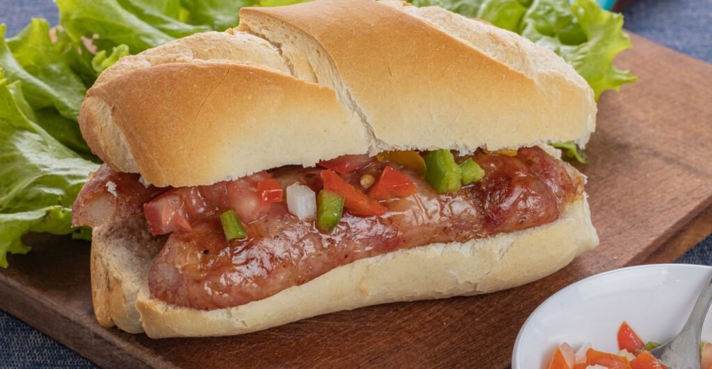Lanchón de chorizo saboroso com pão crocante, servido com acompanhamentos.