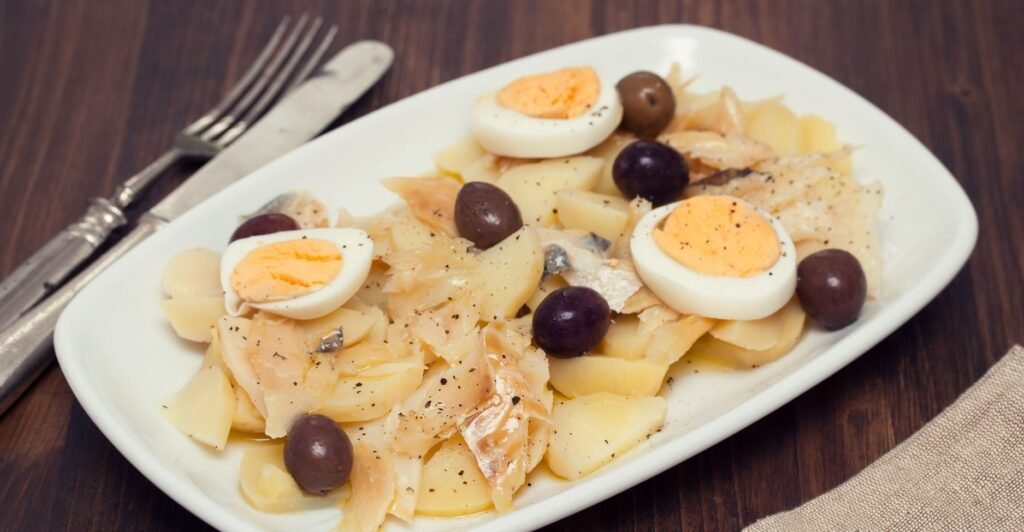 Prato com lascas de bacalhau cozidas, ovos cozidos e azeitonas pretas, decorado e pronto para servir.
