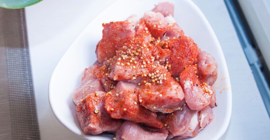 Carne de porco crua sendo marinada com alho, limão e ervas em recipiente de vidro.