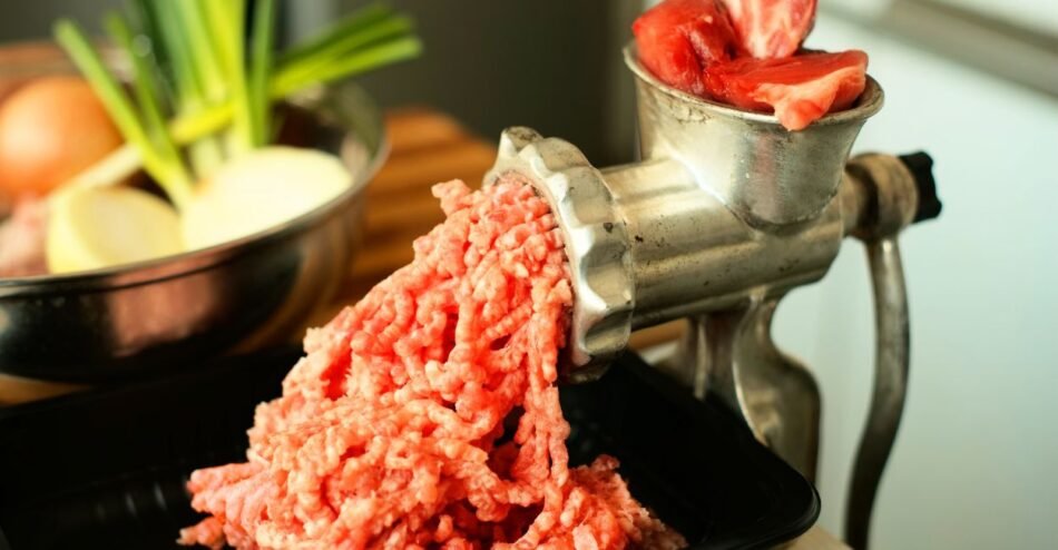 Moedor de carne manual em uso, com carne fresca saindo em tiras.