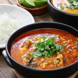 Moqueca capixaba servida em panela de barro com peixe, tomates, cebolas e coentro – comida típica do Sudeste.