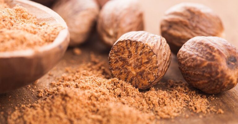 Noz-moscada inteira e ralada em tábua de madeira, mostrando aroma e textura do tempero aromático.