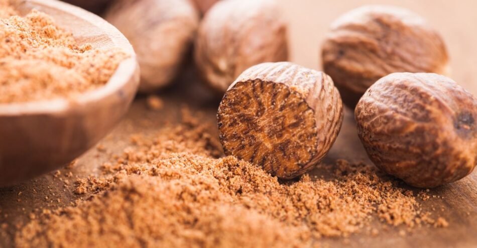 Noz-moscada inteira e ralada em tábua de madeira, mostrando aroma e textura do tempero aromático.