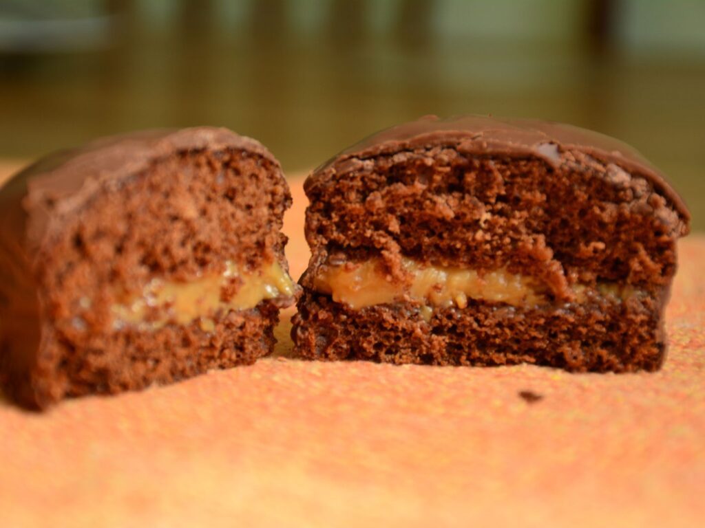 Pão de mel cortado ao meio, mostrando o recheio de doce de leite e a camada de chocolate, disposto em uma tábua de madeira. O pão de mel é um ótimo doce para vender e lucrar.