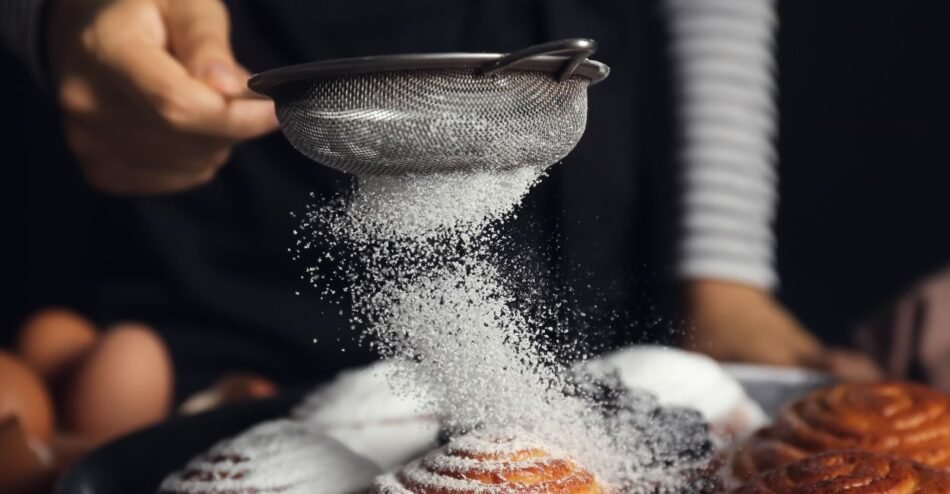 Peneira polvilhando açúcar de confeiteiro sobre fatia de bolo.