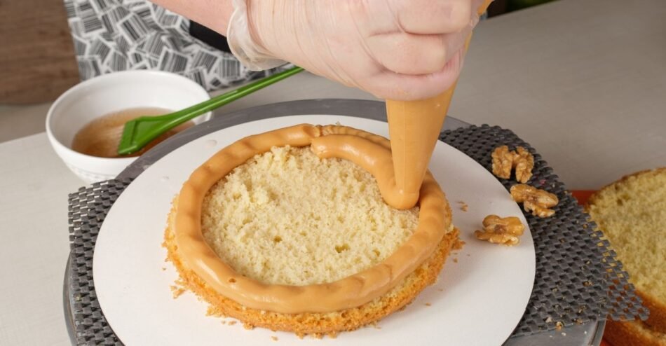 Bolo cortado ao meio sendo recheado com creme branco e frutas frescas.