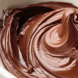 Tigela branca com recheio de brigadeiro para bolo disposto em uma mesa.
