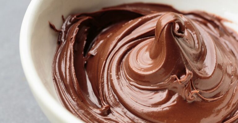 Tigela branca com recheio de brigadeiro para bolo disposto em uma mesa.