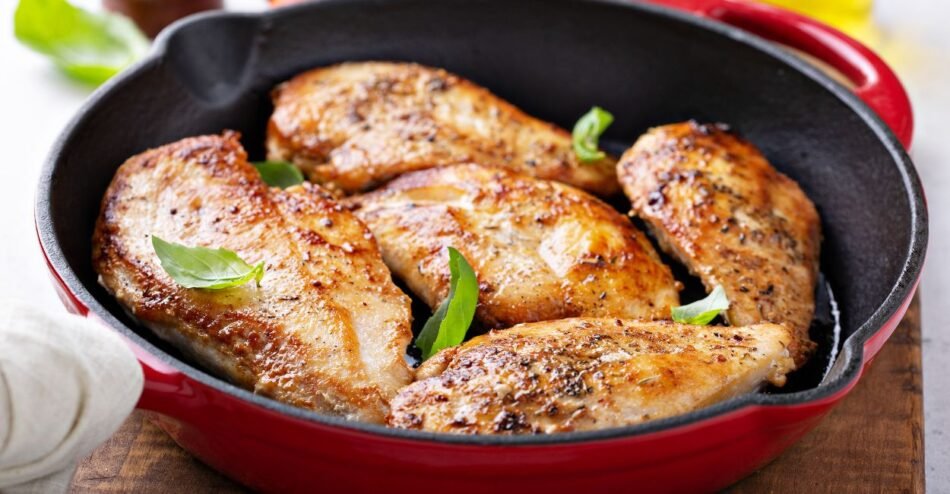 Cubos de frango sendo refogados com cebola e alho em panela larga.
