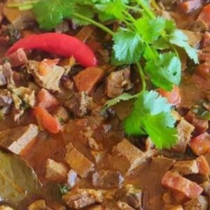Sarapatel servido em panela de barro com molho encorpado e cheiro-verde fresco.