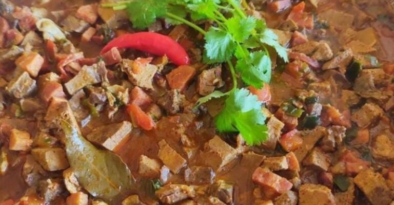 Sarapatel servido em panela de barro com molho encorpado e cheiro-verde fresco.