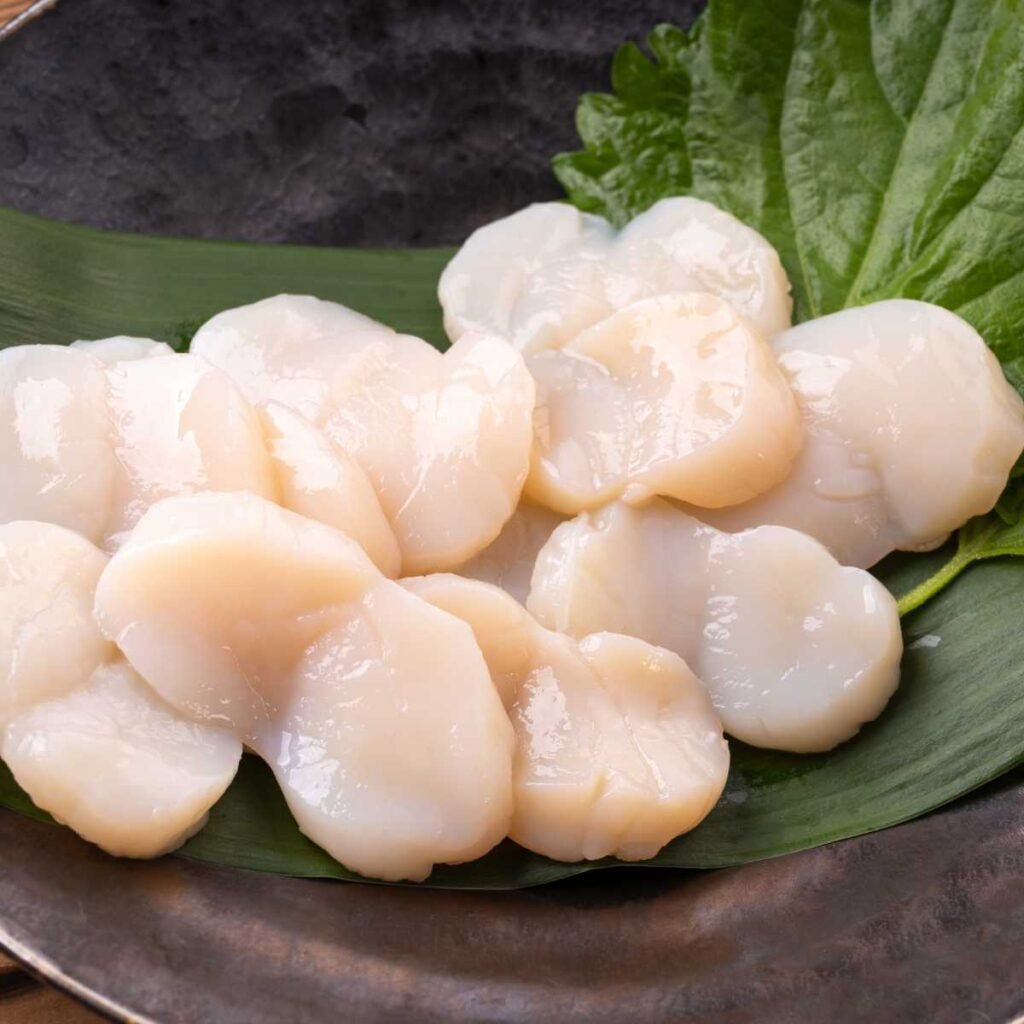 Prato de sashimi de vieira (hotate) com fatias delicadas, acompanhado de wasabi e gengibre.