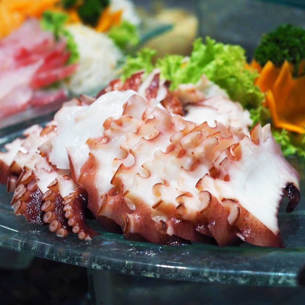 Prato de sashimi de polvo (tako) com fatias finas, acompanhado de wasabi e gengibre.