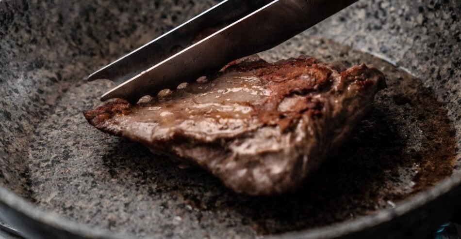 Bife sendo selado em frigideira quente com crosta dourada se formando.