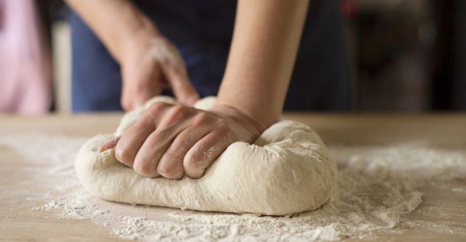Pessoa sovando massa de pão em bancada com as mãos.