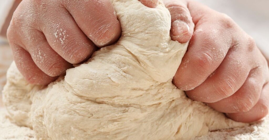 mãos de confeiteiro esticando uma massa elastica para demonstrar a rede de glutén formada pela farinha de trigo.