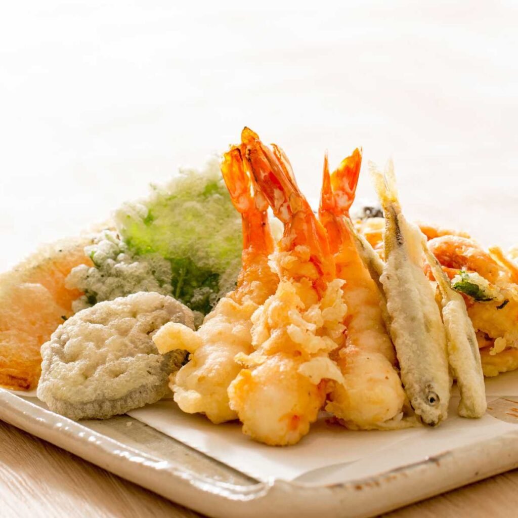 Comida japonesa chamada de tempura, diversos vegetais, peixes e camarões empanados e fritos.