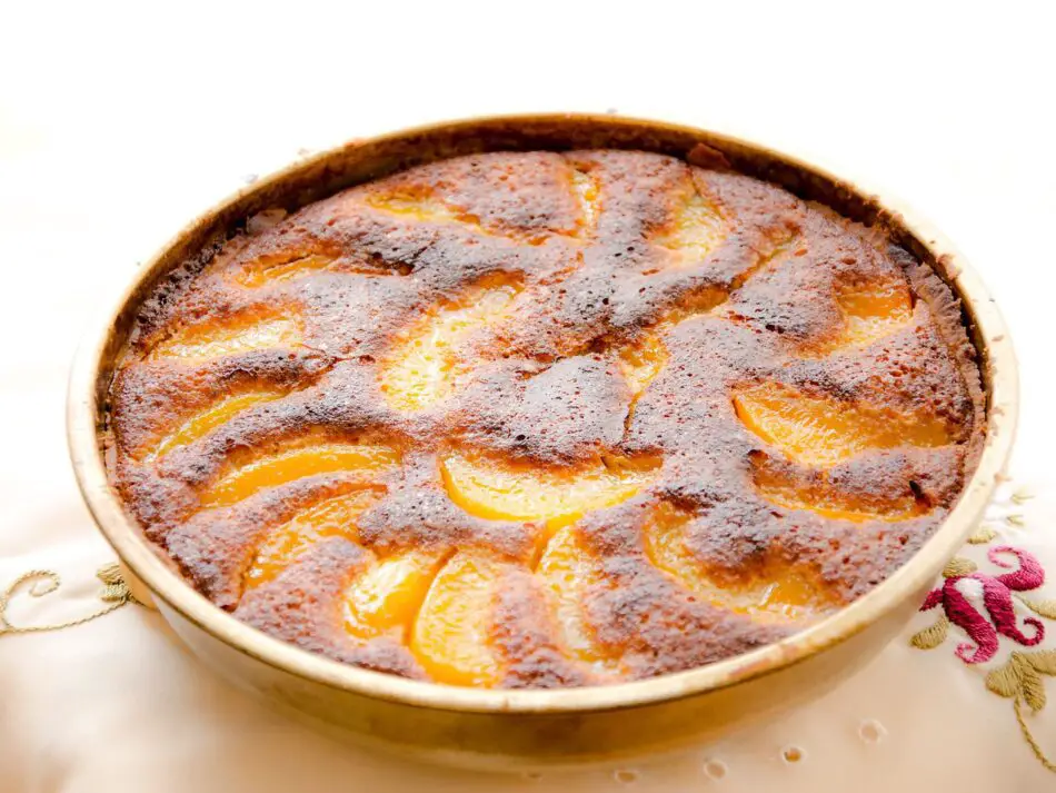 Torta frangipane com recheio de creme de amêndoa e fatias de pêssego douradas no topo.