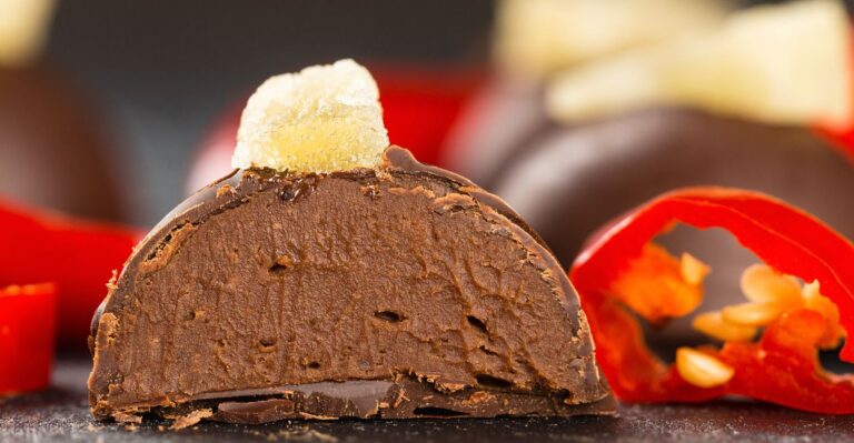 apetitosa trufa de chocolate com pimenta finalizada com cacau em pó e ao fundo pimentas cortadas como decoração.