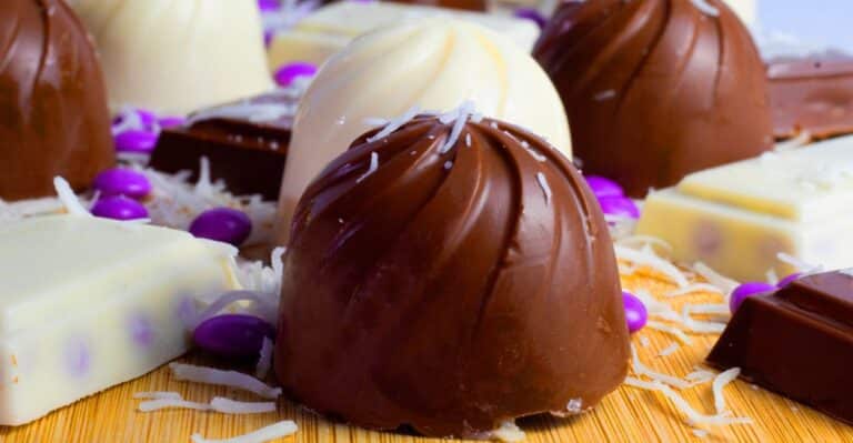 duas trufas de coco, uma finalizada com chocolate ao leite e outra com chocolate branco. raspas de coco por cima.