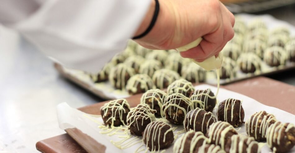 confeiteira finalizando a apresentação de trufas de pistache expostas sobre uma mesa branca.
