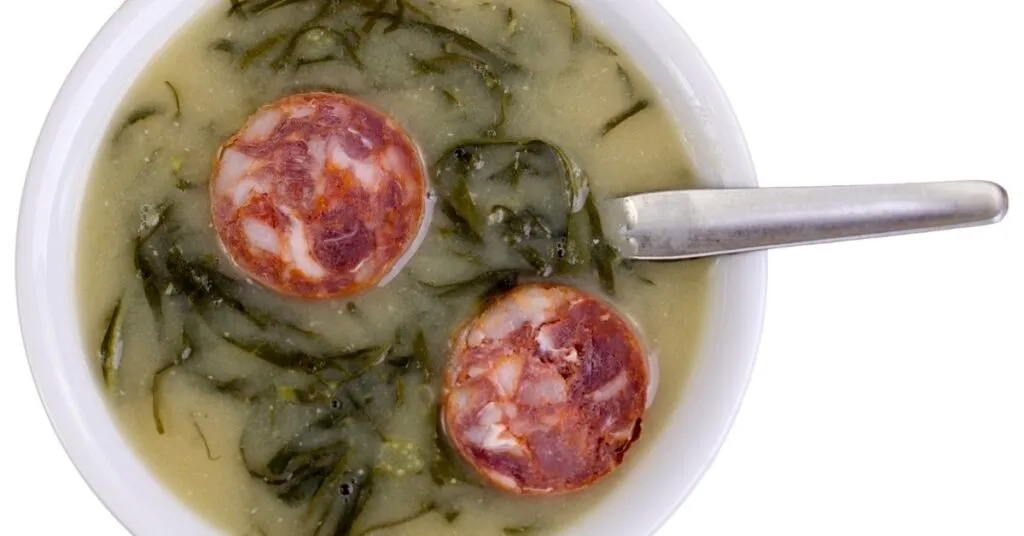 Tigela de caldo verde com couve e pedaços de linguiça, comida de festa junina salgada.