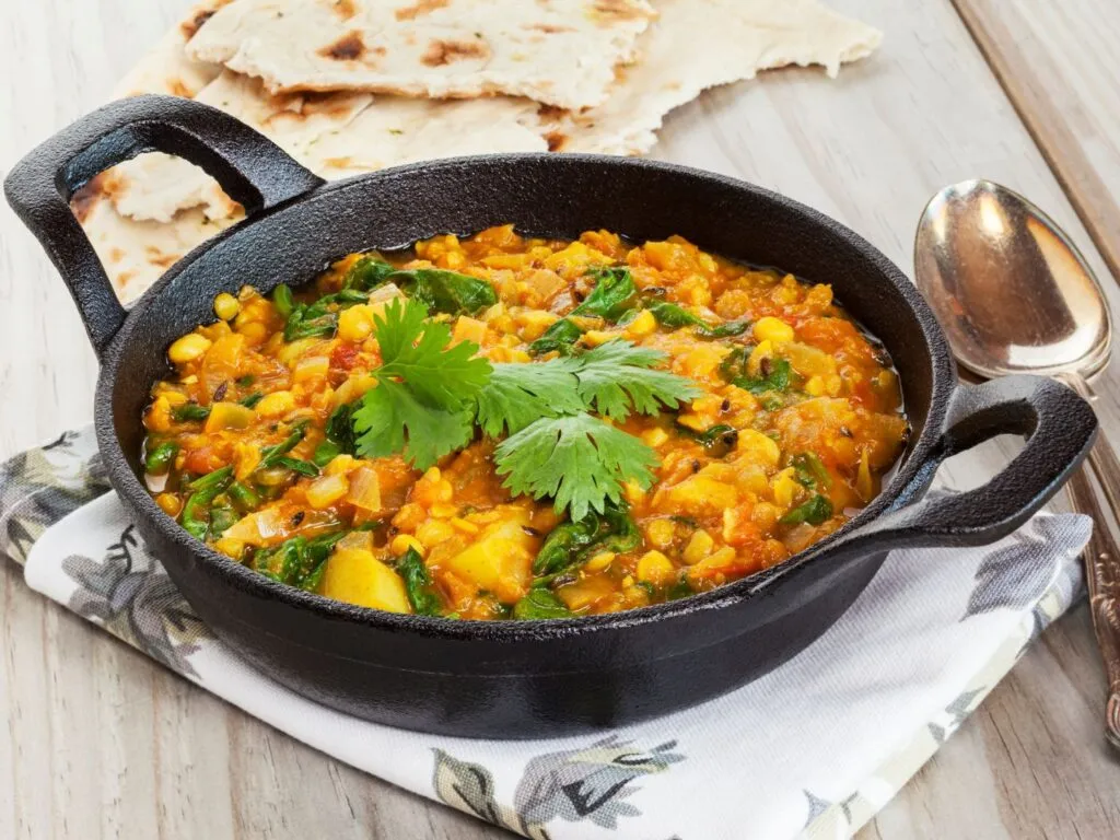 Tigela de dahl indiano, um guisado espesso de lentilhas, decorado com coentro fresco e servido com pão naan ao lado.