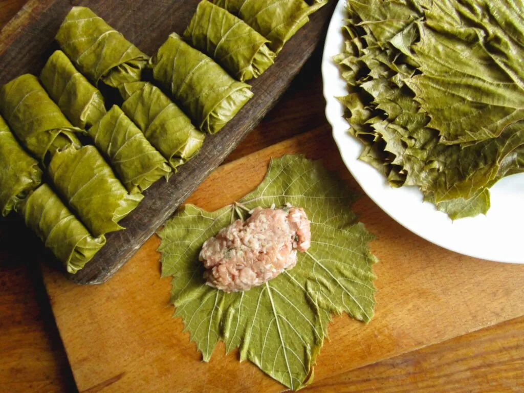 Dolmas de folhas de uva recheadas com arroz, carne moída e especiarias, dispostos em um prato.