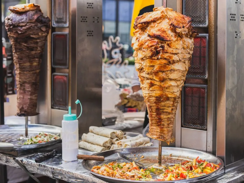 Doner kebab no espeto, com camadas de carne grelhada e bem temperada, girando em um espeto vertical, pronto para ser fatiado.