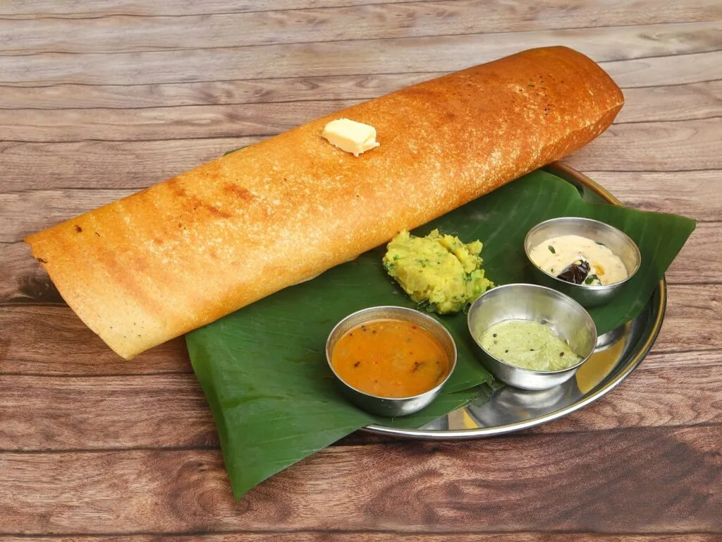 Dosa indiana, uma panqueca fina e crocante, servida com chutneys coloridos e sambar, disposta em um prato tradicional.