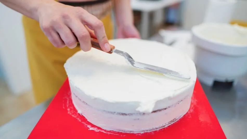 Bolo sendo coberto com glace branco utilizando uma espatula de confeiteiro.