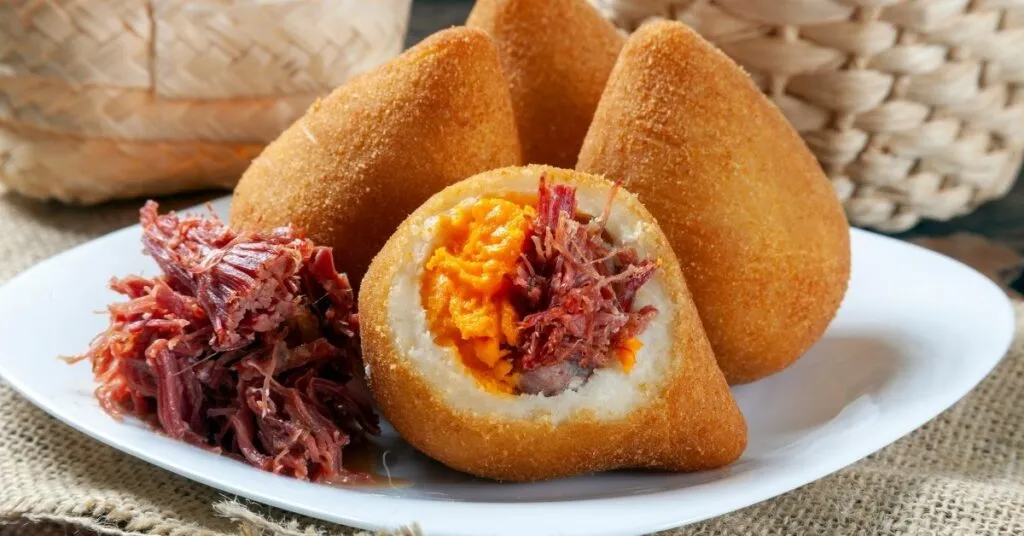 Bolinhos de carne-seca fritos e dourados servidos em cesta típica, comida de festa junina salgada.