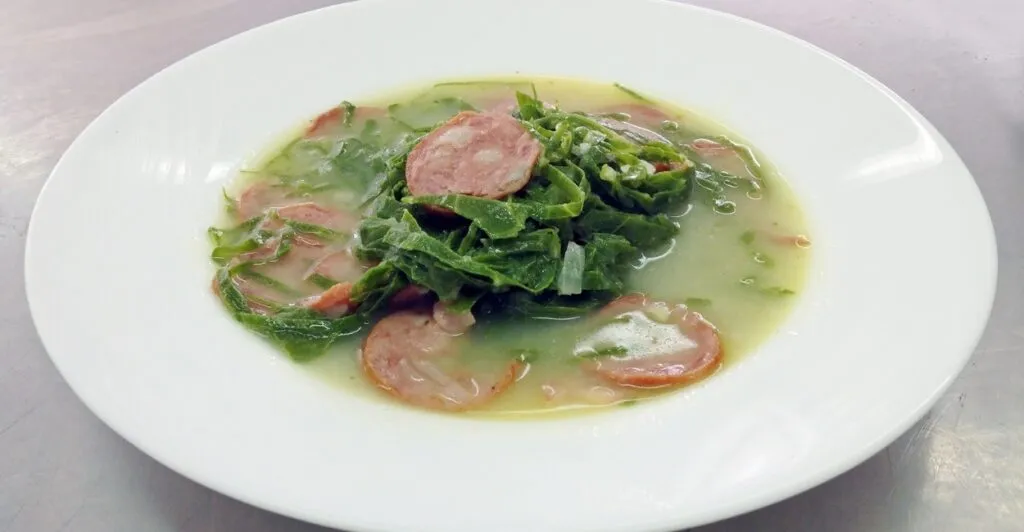 Caldo verde servido em prato branco com rodelas de chouriço, sopa tradicional da culinária portuguesa.