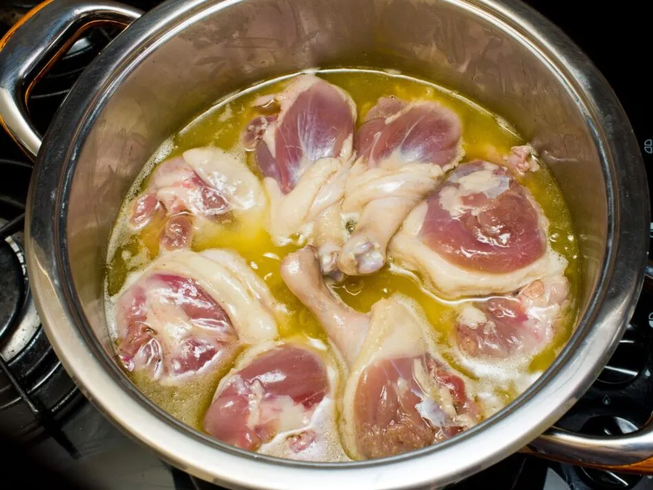Imagem de coxas de pato sendo cozidas lentamente na gordura para preparo de confit.