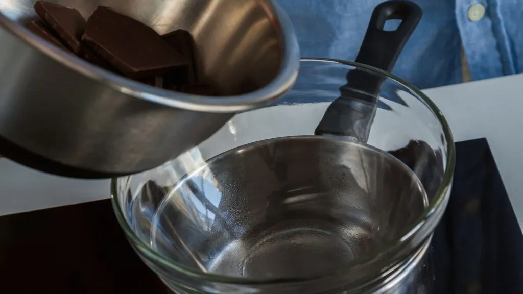 Chocolate sendo derretido em banho-maria, com pedaços de chocolate em uma tigela sobre uma panela com água quente.