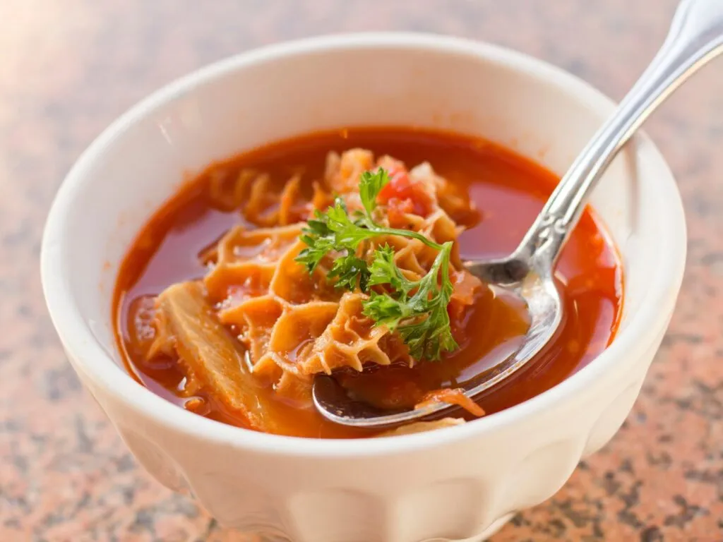 Prato de dobradinha,tradicional prato de comida com D,  com pedaços de bucho de boi cozidos em um molho espesso com feijão branco e vegetais, servido em uma tigela.