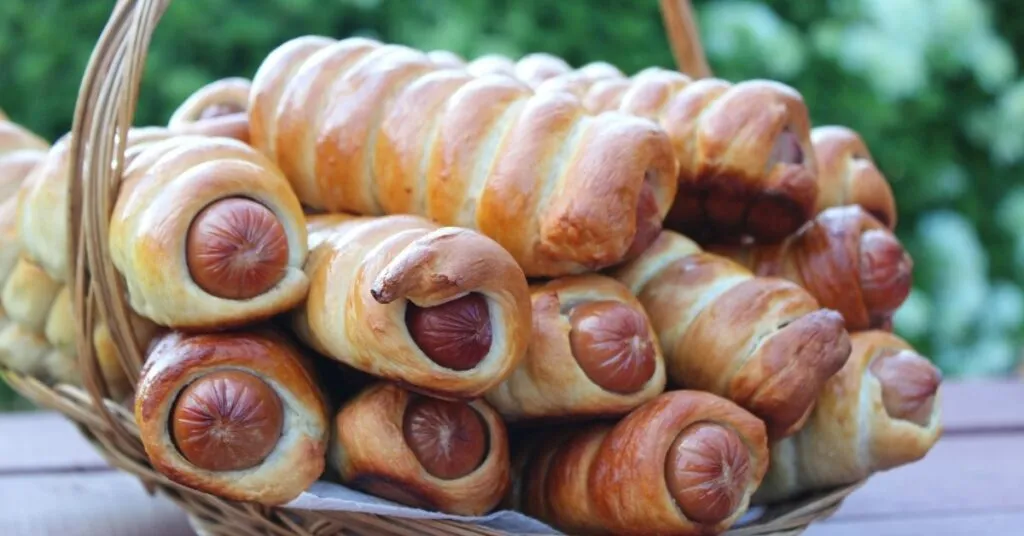 Enroladinhos de salsicha assados com massa dourada, comida de festa junina salgada.