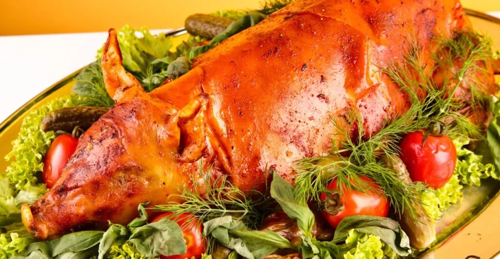 Leitão à Bairrada assado com pele crocante, servido com batatas e laranja, especialidade da culinária portuguesa.