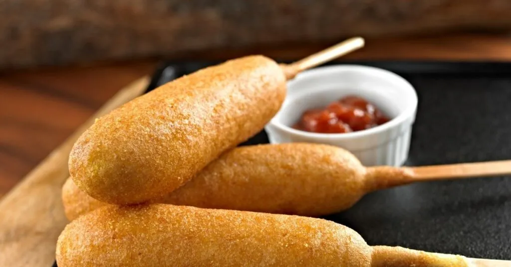 Bolinho de milho no espeto, dourado e servido em estilo rústico, comida de festa junina salgada.