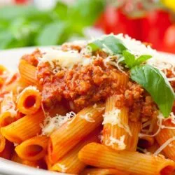 Prato de macarrão penne servido com molho de tomate fresco e manjericão, criando uma refeição leve e saborosa.